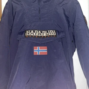 Blå jacka från Napapijri - Säljer en blå jacka från Napapijri. Jackan har en praktisk huva och är tillverkad av syntetmaterial. Perfekt för kyligare dagar. Säljs då jag ej använder den mer.  Vill du veta något mer eller vill ha fler bilder så är det bara att skriva!