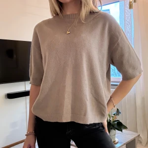 Beige stickad tröja med kort ärm - Säljer en mörkare beige/ljusbrun stickad tröja med korta ärmar och rund hals. Tröjan har en loose passform och ribbade detaljer vid hals, ärmslut och nederkant. Perfekt för dig som gillar en enkel och chill stil. Köptes på arkivet 