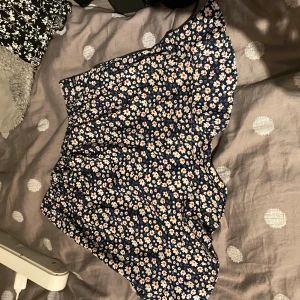 Blommig kortkjol från Seaside - Supersöt kortkjol från Seaside med blå botten och vita blommor med orange detaljer. Kjolen har volangkant och sitter skönt med resår i midjan. Perfekt för dig som gillar blommigt och vill ha en flowy look.