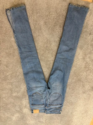 Blå raka jeans från ZARA - Säljer ett par klassiska blå jeans från ZARA med raka ben och fem fickor. Jeansen har hög midja och är tillverkade i slitstarkt denim med snygga detaljer som metallknappar och nitar. Perfekt för dig som gillar en enkel och tidlös look.