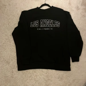 Svart sweatshirt Los Angeles Stories M - Svart sweatshirt från Stories i storlek M med trycket 'Los Angeles California' i vitt framtill. Men då modellen är oversize så passar den även för dig med storlek L och XL.Tröjan har rund hals, ribbade muddar och lång ärm. Perfekt för dig som gillar enkel streetstyle och vill ha en chill vibe. använd ett fåtal gånger.