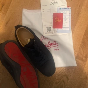 Svarta sneakers från Christian Louboutin - Snygga svarta sneakers från Christian Louboutin med klassisk röd sula och diskret logga undertill. Skorna har rund tå, platt sula och är tillverkade i mjuk mocka med svarta snören. Perfekt för dig som vill ha en lyxig och stilren look.