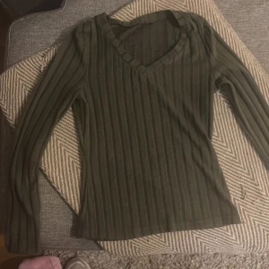 Mörkgrön ribbad långärmad tröja - Tyget ger en bra push:) Snygg mörkgrön långärmad tröja med ribbad struktur och v-ringad hals. Perfekt för dig som gillar stilrena och enkla plagg med lite edge. Materialet känns mjukt och följsamt, och den sitter skönt på kroppen. Passar till jeans eller kjol för en chill look.