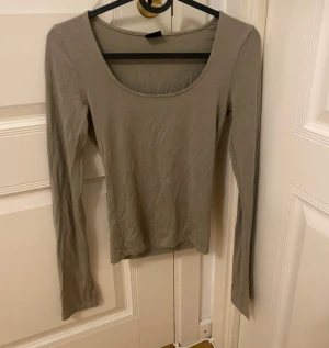Beige långärmad topp Gina Tricot XS - En enkel och stilren grön långärmad topp från Gina Tricot i storlek XS. Toppen har rundad, djup urringning och är figurnära i modellen. Perfekt att matcha med jeans eller kjol för en clean look.