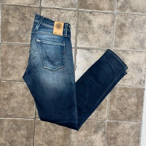 Replay Anbass jeans   - Snygga Replay Anbass jeans i mörkblå tvätt med slitningar och lätt destroyed detaljer på benen. Modellen är skinny fit. Perfekt för dig som gillar en modern och smal siluett. Midja 37cm, längd 102cm. JAG SKICKAR EJ FLER BILDER NÄR JAG BÄR JEANSEN! för storleksguide hänvisar jag till måtten och för bättre inblick i passformen rekommenderar jag att googla på modellnamnet. Jeansen kan vara uppsydda utan att jag noterat det så kolla måtten noggrant :) OBS tyget baktill har börjat tunnas ut. S4 