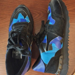 Kom med bud! Valentino Rockrunner sneakers blå/svart - Säljer ett par Valentino Rockrunner sneakers med coolt blått och svart camouflage-mönster. Skorna har snörning, platt sula med nitar på hälen och detaljer i mocka och skinn. Skriv för mer o bättre bilder men även andra frågor, kom gärna med bud också! Görs såklart rena vid köp också. OBS, ingen låda!