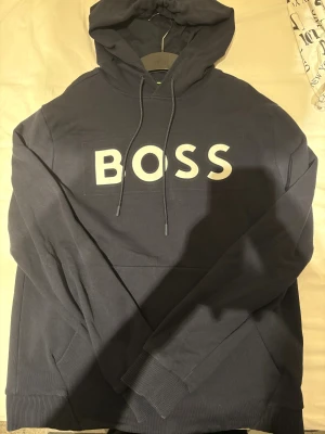BOSS Hoodie - PRIS KAN DISKUTERAS! Mörkblå hoodie från BOSS i bomull med stor vit BOSS-logga på bröstet. Använd fåtal gånger så den är så gott som ny.