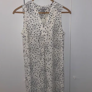 Vit blommig ärmlös klänning H&M - Supersöt vit klänning från H&M med svart blommigt mönster. Ärmlös design och v-ringad hals ger en fräsch och modern look. Lätt och luftig polyester som passar perfekt för varma dagar. Stilren och enkel att matcha med dina favoritaccessoarer.