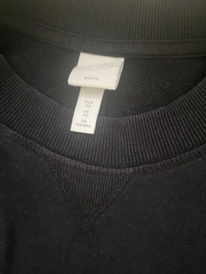 Svart HM basics sweatshirt XS - En enkel svart sweatshirt i klassisk modell från HM BASICS. Tröjan har rund hals, ribbade muddar vid ärmslut och nederkant samt långärmad passform. Perfekt för chill dagar och passar till allt. Materialet är mjuk bomull som känns skönt mot huden.