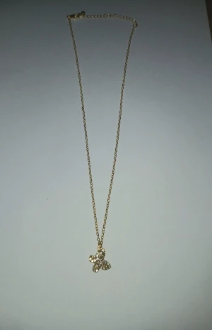 Guldigt halsband med fjärilshänge - Snyggt halsband i guldton med en tunn kedja och ett hänge format som en fjäril. Hänget är dekorerat med glittrande stenar på ena sidan och har en slät, blank yta på andra sidan. Perfekt accessoar för att lyfta din outfit.❤️🦋