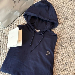 Brunello Cucinelli hoodie - Säljer en marinblå hoodie från Brunello Cucinelli i slim fit-modell. Tröjan är tillverkad i 100% bomull och har långa ärmar samt en liten broderad logga på bröstet. Perfekt för dig som gillar stilrena och exklusiva plagg. Nypris 7k mvh VL