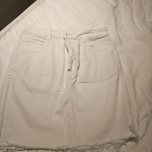 Vit jeanskjol från &Denim, strl 40 - Vit jeanskjol från &Denim i klassisk femficksmodell. Kjolen har rå, fransig kant nertill och dragkedja framtill. Snygg och enkel design som passar till mycket. Gjord i kraftig bomullsdenim för en cool look.