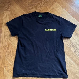 Svart Corteiz t-shirt World Rally Team - Svart t-shirt från Corteiz med trycket 'World Rally Team' i neon-gult på bröstet och en stor oval grafik i blått på ryggen. Klassisk rund hals och korta ärmar. Skön bomullskvalitet och normal passform. Storlek M men passar även S. Priset är inte fast.