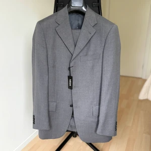 Ljusgrå kostym – Medi, Made in Italy (stl 44) - Snygg ljusgrå kostym från Medi, Made in Italy. Klassisk modell i tunn ullblandning, perfekt för vår och sommar eller som en tidlös businesskostym.  Storlek: 44  Färg: Ljusgrå  Nypris: 3995 kr  Skick: Ny med tags  Lite stor i storleken. Kan passa 44,46,48 beroende på kroppsform. 