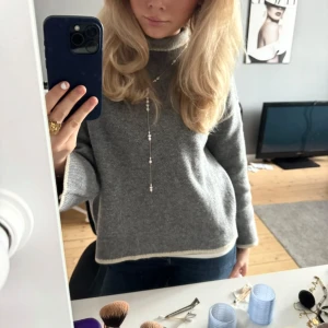 Grå polotröja med vita detaljer från Zara - Säljer en grå polotröja från Zara. Tröjan har en loose passform och är långärmad med hög krage. Materialet är stickat och känns mjukt mot huden. Supersnygg att styla med ett längre halsband som på första bilden. (Endast använd 2ggr)
