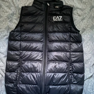 Svart dunväst från EA7 Emporio Armani - Snygg svart dunväst från EA7 Emporio Armani i storlek 160 som konstigt nog sitter som en S - Passar mig som är 180cm. Endast använd 1-2 gånger, och därmed är den i nyskick. Nypris: 2099kr. Mitt pris: 349kr
