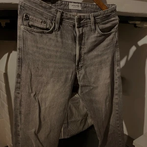 Grå jeans från Jack & Jones - Snygga grå jeans från Jack & Jones med klassisk femficksdesign och bälteshällor. Jeansen har en rak passform och är tillverkade i slitstarkt bomullsmaterial. Perfekt för dig som gillar en enkel och stilren look.