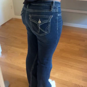 Mörkblå bootcut jeans med kontrastsömmar - Snygga mörkblå jeans med bootcut passform och tydliga vita kontrastsömmar. Jeansen har klassiska fickor fram och bak, där bakfickorna har dekorativa sömmar och knappdetalj. De sitter så fint på kroppen och är gjorda av denim material