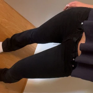 Svarta bootcut jeans med fickdetalj - Säljer ett par svarta jeans med bootcut-snitt och snygga fickor bak med silverknapp. Jeansen har normal passform med denim material. Perfekta för dig som gillar klassisk stil med en twist.