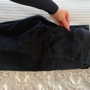Levis 501 jeans straight fit svarta - Säljer ett par svarta Levis 501 jeans med klassisk straight fit och hög midja. Jeansen har knäppning med knappar framtill, fem fickor och den ikoniska röda Levis-taggen på bakfickan. Tillverkade i slitstarkt bomullstyg.