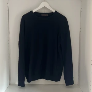 Mörk blå stickad tröja Oscar Jacobson - Klassisk svart stickad tröja från Oscar Jacobson i storlek L. Tröjan har rund halsringning, långa ärmar och ribbade muddar. Perfekt för dig som gillar en stilren och enkel look med premiumkänsla. Sitter som en stor M.