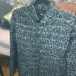 Leopardmönstrad pufferjacka Gina Tricot - Säljer en snygg pufferjacka från Gina Tricot i storlek 40. Jackan har ett grått och svart leopardmönster, hög krage och knäppning framtill. Perfekt för dig som vill sticka ut med en cool look under höst och vinter.