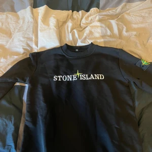 Svart Stone Island sweatshirt - (BARNSTORLEK) Svart sweatshirt från Stone Island i storlek 152, med broderad logga på bröstet och klassisk patch på ärmen. Tröjan har rund halsringning och långa ärmar. Perfekt för dig som gillar streetwear och vill ha en clean look. Priset kan diskuteras vill bara få den såld. 