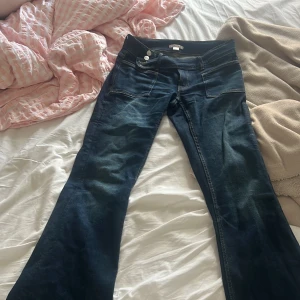 Mörkblå bootcut jeans från Gina Tricot - Snygga mörkblå jeans från Gina Tricot med bootcut passform och hög midja. Jeansen har stora framfickor, dubbla knappar i midjan och klassiska kontrastsömmar. Perfekta för dig som gillar en retroinspirerad look med lite utsvängda ben.