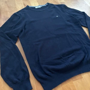 Mörkblå tröja från J.Lindeberg S - Klassisk mörkblå tröja från J.Lindeberg i storlek S. Tröjan har rund halsringning, diskret logga på bröstet och ribbade muddar vid ärmslut och nederkant. Perfekt för en stilren och enkel look.