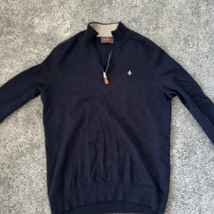 Marinblå merinoulltröja från Morris - Snygg marinblå tröja från Morris i 100% merinoull. Tröjan har half zip med läderdetalj, lång ärm och diskret logga på bröstet. Perfekt för dig som gillar klassisk stil med modern touch.