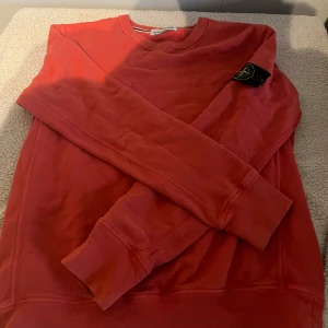 Röd Stone Island sweatshirt - Säljer en röd sweatshirt från Stone Island med klassisk logga på ärmen. Tröjan har rund halsringning, långa ärmar och ribbade muddar. Perfekt för dig som gillar streetwear eller grisch och vill sticka ut med en snygg färg. Materialet är mjukt. 