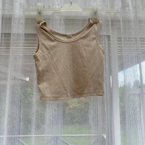 Beige ribbad linnetopp - Säljer en beige, croppad linnetopp med ribbad struktur. Toppen är ärmlös och har en rund halsringning. De är nått ljusblått märke på sidan av ena armen som man ser på bild 2. Därav 10kr
