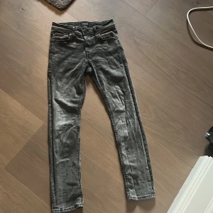 Svarta slim jeans Jack & Jones - Snygga svarta slim fit jeans från Jack & Jones, modell Glenn. Jeansen har en tvättad look med gråa nyanser, klassiska fem fickor och smal passform. Perfekta för dig som gillar en modern och stilren vibe.