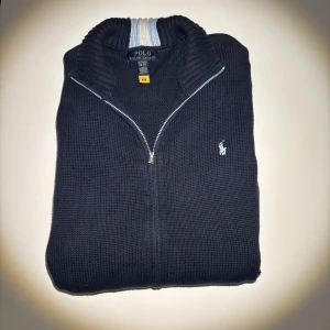 Mörkblå stickad kofta Polo Ralph Lauren - Snygg mörkblå stickad kofta från Polo Ralph Lauren med dragkedja och ribbad krage med vit och ljusblå rand. Klassisk logga broderad på bröstet och två fickor framtill. Perfekt för lager-på-lager och chill stil. Priset är inte hugget i sten☺️