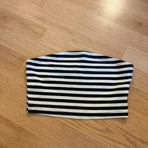 Randig bandeau tubtopp från SHEIN - Säljer en svartvit randig bandeau tubtopp från SHEIN i storlek XS. Toppen är ribbad och har en enkel, ärmlös design som sitter tight mot kroppen. Perfekt för att skapa en cool och avslappnad look till sommaren.