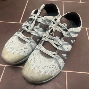 Ljusblå hiking sneakers  från Merrell - Säljer ett par ljusblå sneakers från Merrell med grå detaljer och snörning. Ovandelen är i mesh och syntet, vilket gör dem riktigt lätta och andningsbara. Sulan har grovt mönster för extra grepp, perfekt för dig som gillar att vara aktiv utomhus. Storlek 27cm