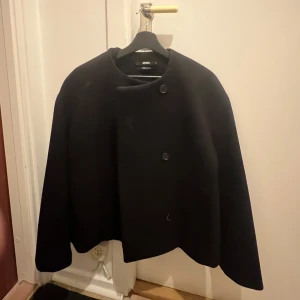 Svart rock från Bik Bok med knappar - Stilren svart rock från Bik Bok med minimalistisk design och tre stora knappar framtill. Jackan har en rak, något boxig passform och är tillverkad i ett tjockare material som passar perfekt för kyligare dagar.