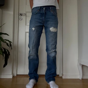 Levi's 501 blå jeans med slitningar - Säljer ett par ursnygga blå Levi's 501 jeans med raka ben och snygga slitningar, storlek W29 L32. Dessa var några av mina favvojeans men har tyvärr vuxit ur dom 💔Sjukt balla och passar verklgien till allt! Jeansen e fortfarande i superbra skick men har slitits lite nere vid anklarna (syns på sista bilden). Skriv för mått eller fler bilder!