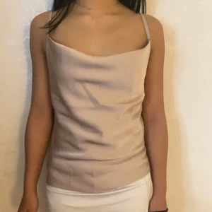 Champagnefärgad linnetopp i satin - Säljer en stilren champagnefärgad linnetopp med tunna axelband och snygg draperad halsringning. Toppen har en slät, glansig satinfinish som ger en lyxig känsla och passar perfekt till både jeans och kjol. Enkel men ändå supertrendig för dig som gillar minimalistisk stil.