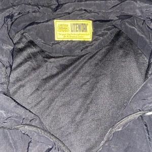 Corteiz svart och vit vindjacka - Säljer en Corteiz vindjacka i svart och vitt med huva och dragkedja. Jackan har reflekterande detaljer längs axlarna och är tillverkad i lätt polyester. Perfekt för dig som vill ha en stilren och sportig look med streetkänsla.