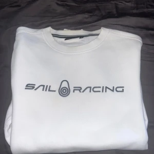 Vit Sail Racing sweatshirt i bomull - Vit sweatshirt från Sail Racing med broderad logga framtill. Klassisk rund halsringning och stilren design. Perfekt för dig som gillar sportig och clean stil. Tillverkad i mjuk bomull för skön känsla hela dagen.