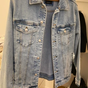 Ljusblå jeansjacka från Zara - Snygg ljusblå jeansjacka från Zara med klassisk passform. Jackan har två bröstfickor med knappar, silverfärgade detaljer och raka sömmar. Perfekt att slänga över en hoodie eller t-shirt för en chill look.