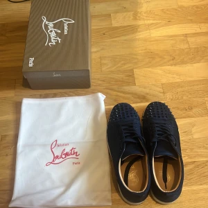 Mörkblå Christian Louboutin sneakers - Snygga mörkblå sneakers från Christian Louboutin med klassiska röda sulor och coola nitar framtill. Ganska många nitar borta men inget märkvärdig, köpta för 4000, säljer för 2000, hör av er vid frågor😃