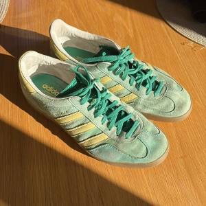 Adidas Samba i mintgrön mocka - Adidas Samba sneakers i mintgrön mocka med klassiska gula ränder och detaljer. Skorna har gröna snören, vit insida och gummisula. Perfekt för dig som vill sticka ut med en retrovibe och snygga färgkombos.