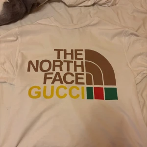 Vit Gucci x The North Face t-shirt S - Exklusiv vit t-shirt från Gucci x The North Face med stor färgglad logga på ryggen i brunt, gult, grönt och rött. Klassisk rund hals och korta ärmar. Tillverkad i mjuk bomull, perfekt för dig som gillar statement-plagg och designer. Använd bara 3 gånger