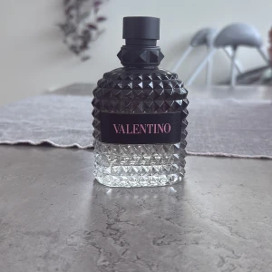 Valentino parfym med nitar - Snygg parfymflaska från Valentino med svart och transparent glas i ett coolt nitat mönster. Flaskan har svart kork och etikett med rosa text. Perfekt för dig som gillar lyxiga och trendiga dofter. Rymmer ungefär 86-87 ml kvar av 100