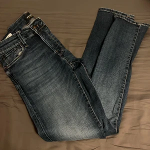 Mörkblå jeans från Jack & Jones 29/32 - Snygga mörkblå jeans från Jack & Jones i klassisk femficksmodell. Jeansen har en lätt tvättad look med kontrastsömmar och normal passform. Perfekta till sneakers eller boots och funkar året runt.