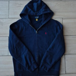 Marinblå hoodie från Polo Ralph Lauren - Snygg marinblå hoodie från Polo Ralph Lauren med dragkedja och huva. Sparsamt använd, inga fläckar, eller defekter i allmänhet. Storlek S. Nypris runt 1500. Vi säljer för 800. Tveka inte att höra av er med funderingar eller prisförslag!
