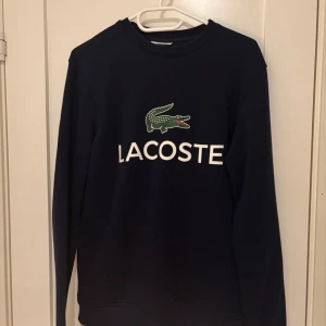 Lacoste sweatshirt - Säljer en fet blå Lacoste sweatshirt i storlek S köpt för 1399 kr på Åhléns använt några ynka få gånger, skicket är som nytt. Säljer den pga att jag bränt alla mina pengar på casino i helgen och behöver deg för att klara månaden. För en snabb och smidig affär kan priset diskuteras!