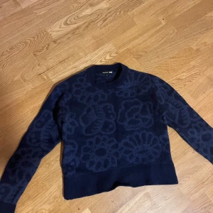 Mörkblå blommig tröja Marimekko x Uniqlo - Säljer en mörkblå stickad tröja från Marimekko x Uniqlo i storlek S. Tröjan har ett snyggt blommigt mönster ton-i-ton, rund halsringning och långa ärmar. Perfekt för dig som gillar unika prints och vill ha något extra i garderoben.